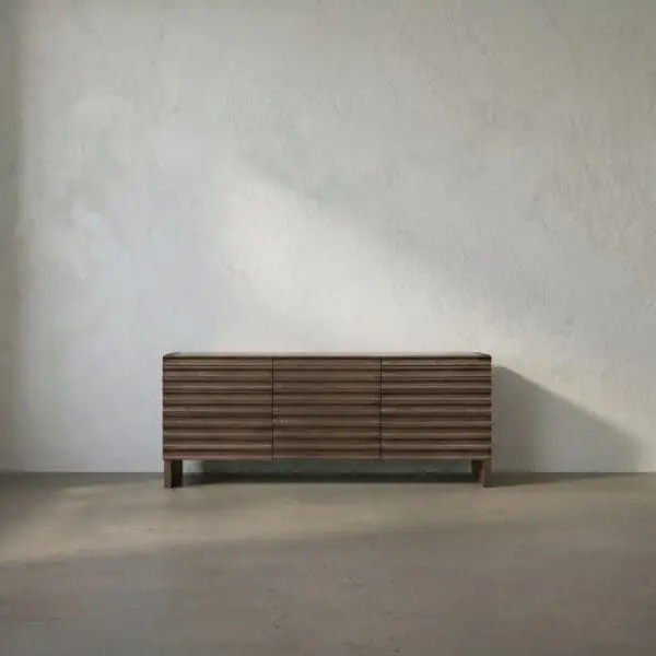 Walnut wood sideboard with horizontal slats against a light textured wall in a minimalist room.