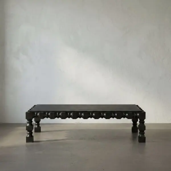 Low, black wooden bench with carved legs placed on a concrete floor against a light textured wall